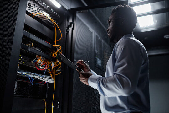 Backlit side view portrait of black man working with server cabinet in data center and taking notes on clipboard, copy space