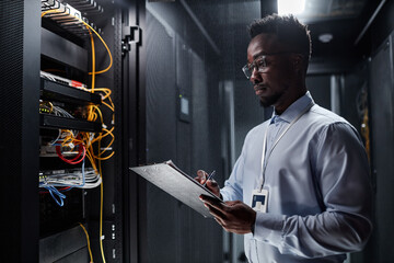 Fototapeta Waist up side view portrait of network engineer working with server cabinet in data center and taking notes on clipboard, copy space obraz