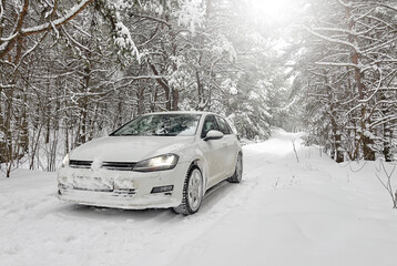 White car on a snowy road in the forest