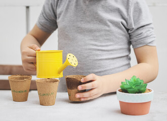 A little caucasian girl with a gray turtleneck holds a yellow watering can with her hands and waters cardboard glasses