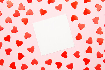 Mockup paper greeting card or wishes card on pink background. Pattern of red hearts, fountain pen for writing greeting and wishes, top view.