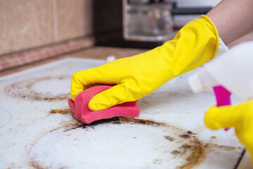 Man cleaning ceramic modern stove or hob with detergent agent. Hand in yellow gloves clean stove...
