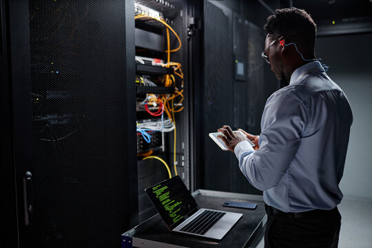 Side view portrait of network engineer using laptop while setting up servers in data center