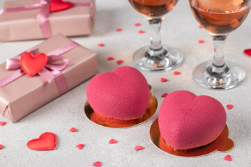 Homemade bright mousse cakes Hearts with pink velvet coating and two glasses of rose wine on light background