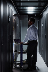 Vertical full length portrait of black man as network engineer using laptop and setting up servers in data center