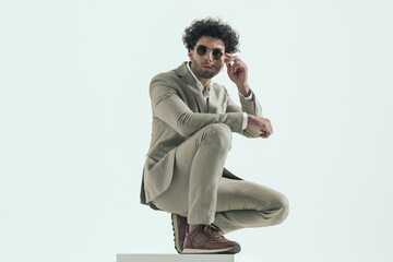 fashion man in suit with curly hair adjusting sunglasses and posing