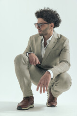 sexy businessman with curly hair holding elbows on knees and posing