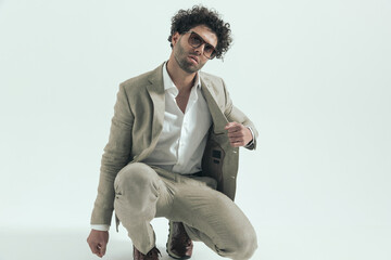 cool fashion arabic man with sunglasses crouching and pulling suit