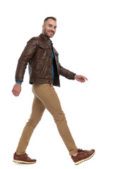 side view of happy guy in brown leather jacket smiling and walking