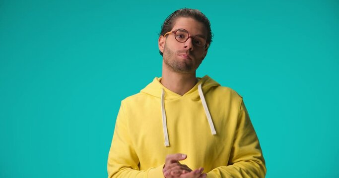 bored young man with glasses wearing yellow hoodie and applauding the boring show on blue background