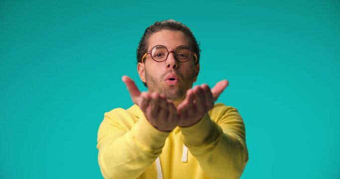 project video of sexy man with glasses smiling, flirting and sending kisses in front of blue background in studio