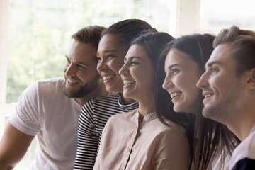 Obraz premium Diverse united team sitting close in line, looking away, smiling, laughing, posing for shooting, celebrating teamwork success. Multiethnic friends enjoying leisure, friendship