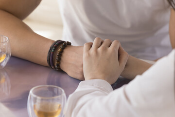 Young couple holding hands over tabletop, meeting in cafe, flirting, enjoying romantic leisure, time, dating, drinking tea. Girl friend touching arm of man with love, carte, support