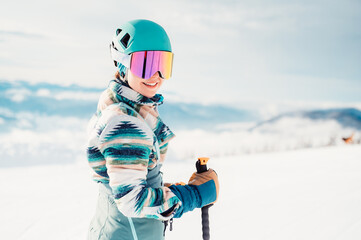 Woman in skiing clothes with helmet and ski googles on her head with ski sticks. Winter weather on the slopes. Mountain and enjoying view. Alpine skier. Winter sport. Ski touring - obrazy, fototapety, plakaty
