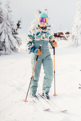 Woman in skiing clothes with helmet and ski googles on her head with ski sticks. Winter weather on...