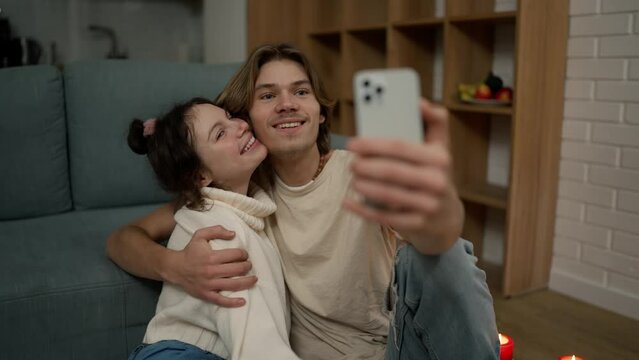 Lovely couple sitting on the floor together, taking selfie with smartphone