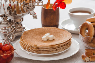 Russian traditions. Russian holiday Maslenitsa. Still life with a cup of tea, a stack of pancakes, sour cream, honey, cubes of butter, bagels, dried fruits, caramel cockerel and samovars.