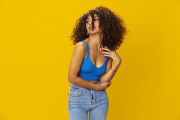 Woman with curly afro hair in a blue t-shirt on. yellow background signs with her hands, look into the camera, smile with teeth and happiness, copy space