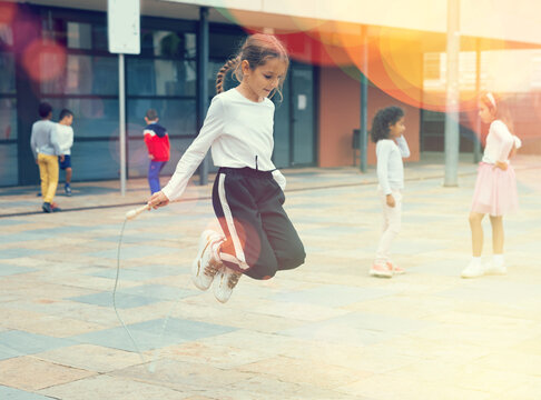 Cheerful sporty tween girl jumping rope in school yard during recess in warm autumn day