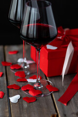 Saint Valentine's Day celebration. Wineglasses with red wine, hearts, gift box, postcard on dark wooden background. Happy holiday . Table decor for festive dinner, romantic atmosphere
