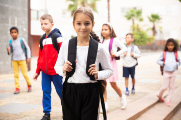 Obraz premium Portrait of tweenager girl with backpack walking with other schoolchildren to school campus after lessons on warm fall day.