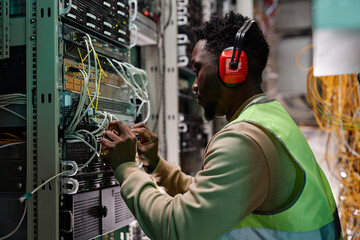 Side view portrait of young technician setting up network in server room and wearing protective...