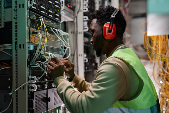 Side view portrait of young technician setting up network in server room and wearing protective workwear