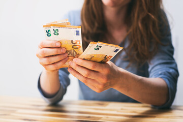 Caucasian woman with red hair counting Euro banknotes at a table at home