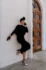 Stylish woman in the city. Fashion photo of a beautiful model in an elegant black dress posing against the backdrop of a building on a city street