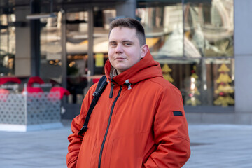 Street portrait of a young man 20-25 years old on a blurry background of a modern European building, people pass by.