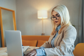 Young beautiful blonde businesswoman or college student works on laptop at home or in office. Online seminar, distance learning or job concept.