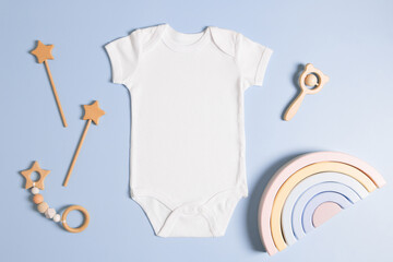 White cotton baby short sleeve bodysuit and natural wooden toys on light green background. Infant onesie mockup. Blank gender neutral newborn kid bodysuit mock up template. Top view