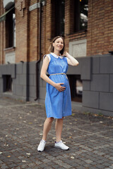 Happy pregnant woman chilling and having fun while walking in the city in a midi blue vintage dress. Happiness all around