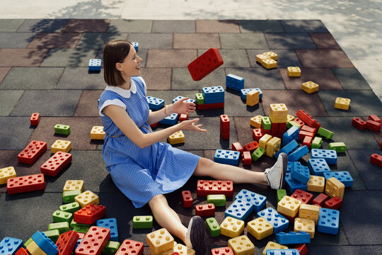 A beautiful pregnant woman in a blue dress playing with big colorful cubes on a children playground while sitting and watching the cubes. Pregnancy creative concept