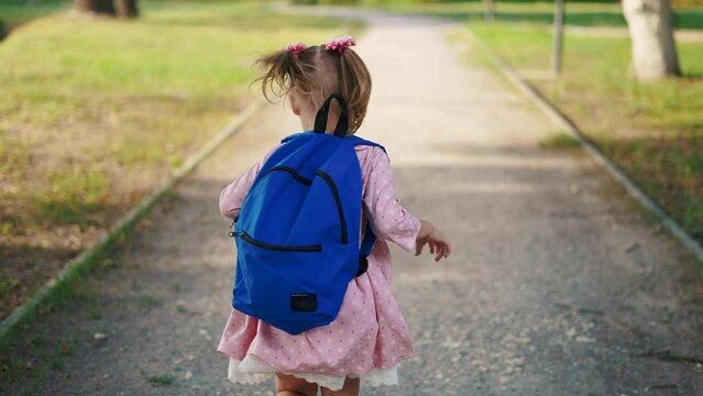 back to school. a little girl with a backpack runs through the green park to school along the path. education kid dream concept. a small child with a backpack back view runs the park to school sun