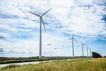 Wind turbines on the bank of a canal in the countryside on a partly cloudy summer day