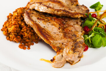 Appetizing grilled pork loin chops with stewed lentils, greens and berries