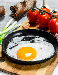 Fried egg in a pan with tomatoes and green onions.