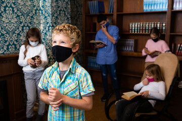 Pensive tween boy in protective mask solving puzzles in escape room with friends. New norms in...