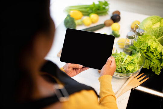 Young african american chef lady in apron cuts salad, use tablet with blank screen at table with vegetables