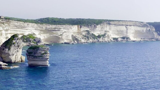 Stack of the Grain of Sand ("U Diu Grossu" in Corsican) of Bonifacio (Corsica, France), a big rock in the blue sea, and huge rocky cliffs in the Accore coast, beautiful holidays touristic landscape