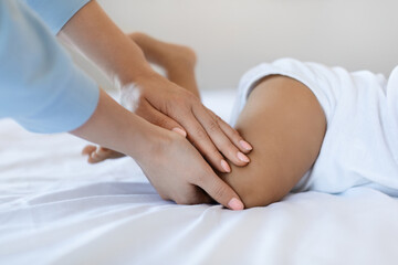 Infant Massage. Unrecognizable Mother Massaging Legs Of Little Black Baby At Home
