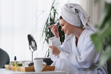 Portrait of a young beautiful woman wearing a bathrobe at home. doing her daily skincare routine with  natural cosmetics