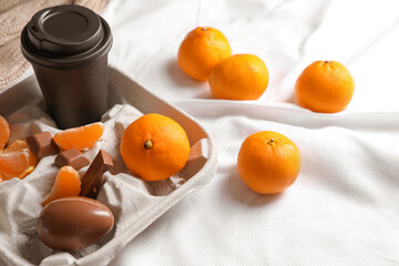 Delicious ripe tangerines, cup with drink and chocolates on white bedsheet