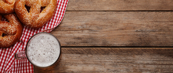 Tasty pretzels and glass of beer on wooden table, flat lay with space for text. Banner design