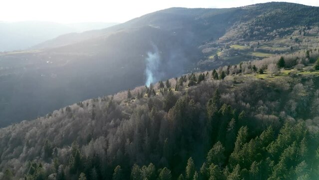 Aerial drone panoramic view passing through a thick cloud of smoke from a wood fire in the forest in cold winter with many green pine and spruce trees, dangers of an arsonist starting a fire