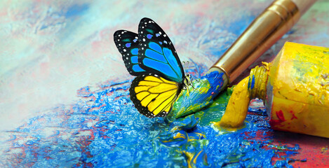 color concept. colorful tropical morpho butterfly on an artist's palette with a brush and strokes of oil paint