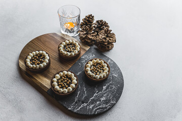 Four mini chocolate dessert tarts served on wooden and stone tray on stone table with candle and decorative pinecones. Festive winter desserts. Horizontal shot. High quality photo