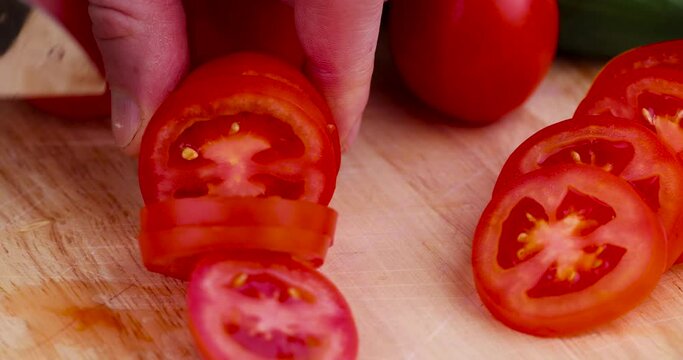 Slicing red ripe tomatoes with a knife on a board, ripe fresh tomatoes while slicing into pieces