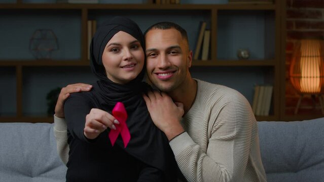 Multiracial family muslim woman and african american man sit on sofa indoors hold red ribbon prevent symbol HIV AIDS protect immune deficiency syndrome blood donation health care and world cancer day